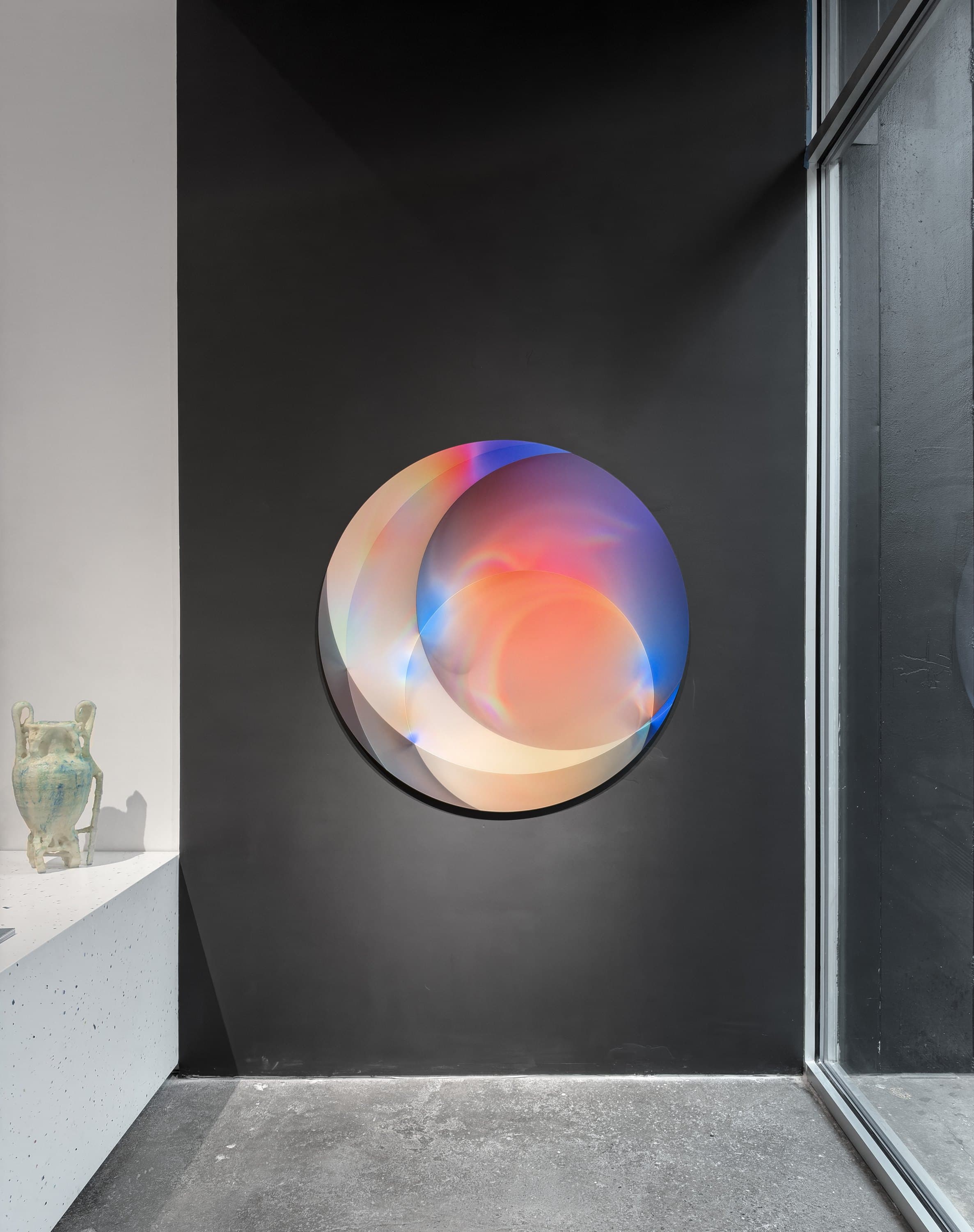 The circular Dispersion Disk Study on a black wall beside the gallery window.