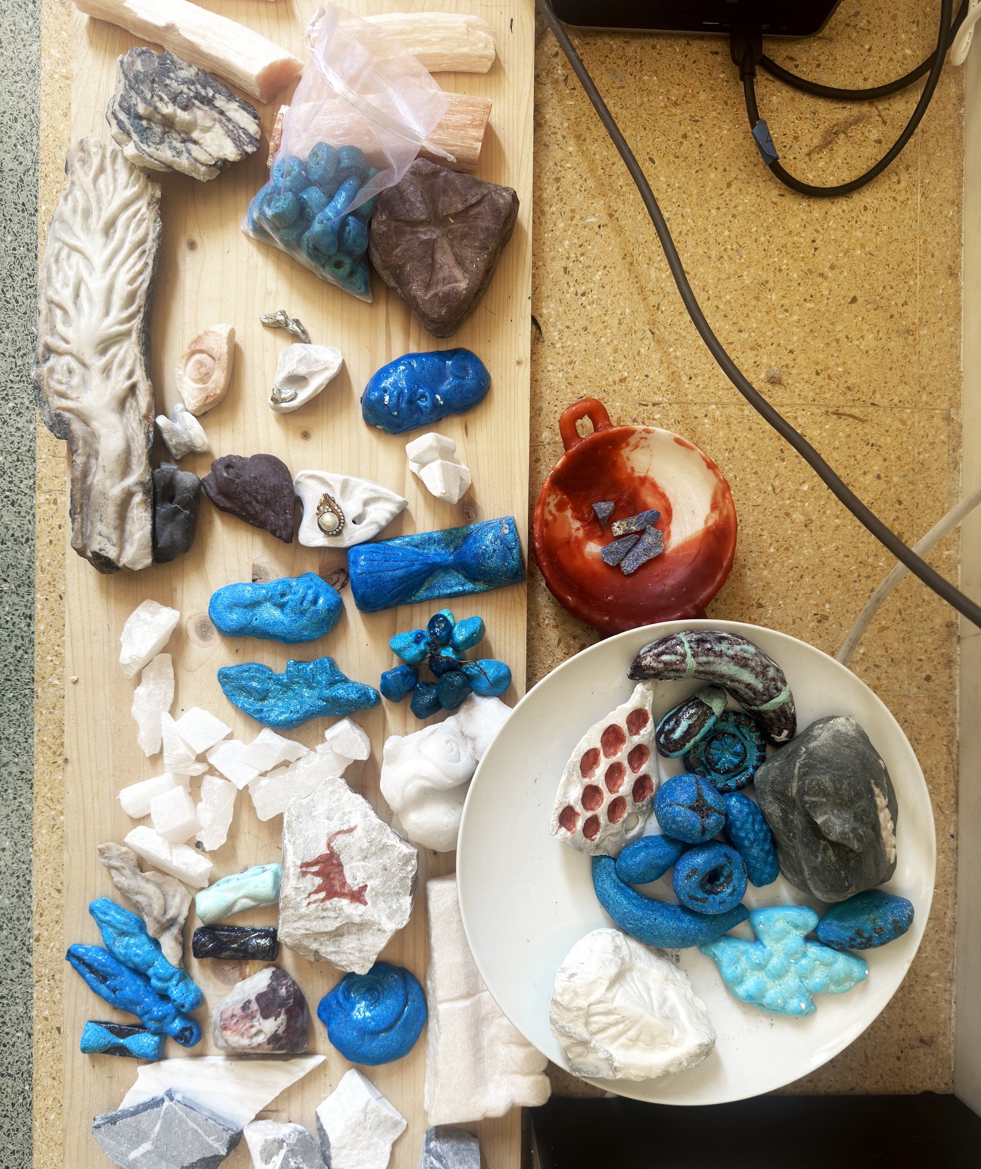 Many Amulets laid out on a board, in marble, ceramic and glazed forms.